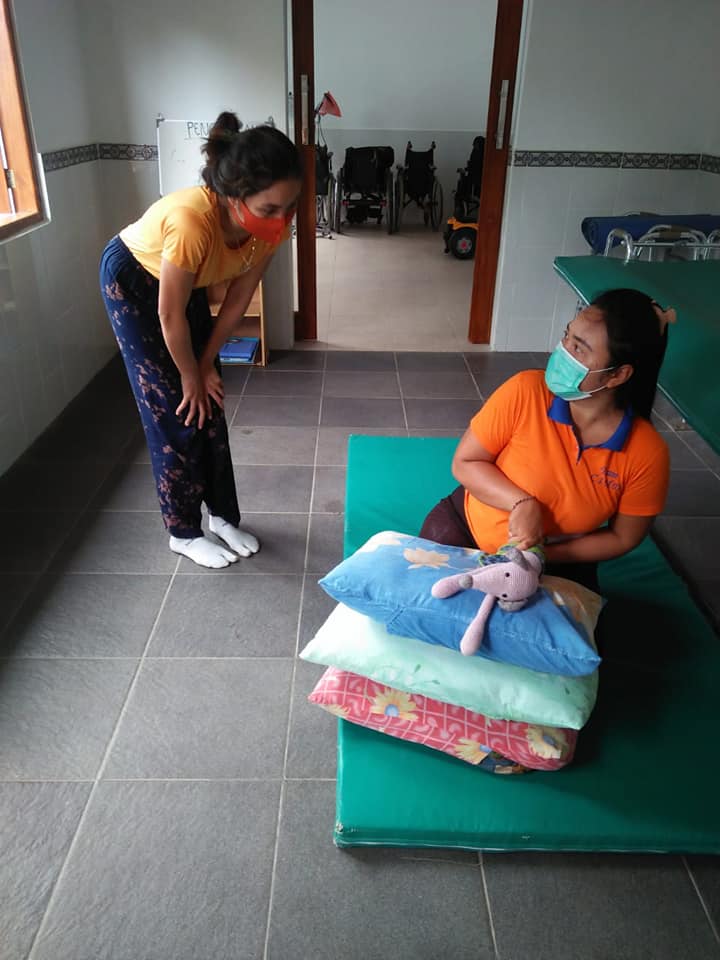 A physiotherapist demonstrating a technique to a parent using pillows and a stuffed animal.